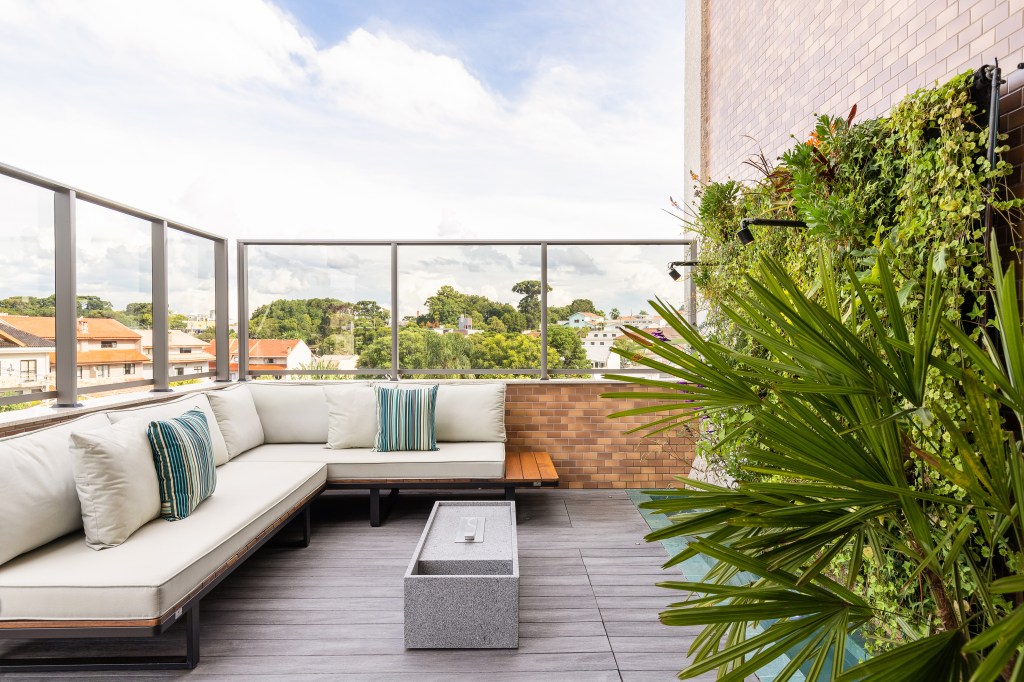 Terraço; varanda com sofá, deck de madeira, parede de pedras e jardim vertical.