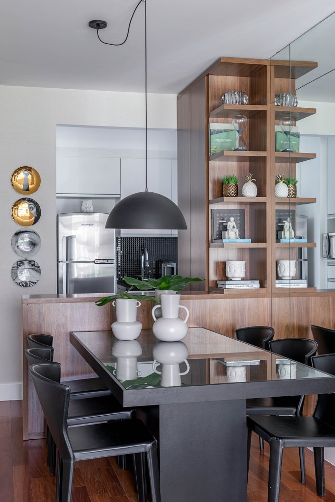 Sala de jantar integrada com cozinha; estante em marcenaria escura que funciona como divisão e bancada entre os dois ambientes.