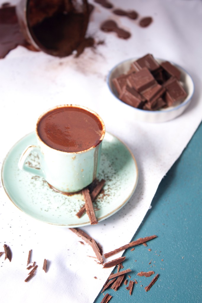Xícara de cerâmica com chocolate quente cremoso e tigela com chocolate em barra.
