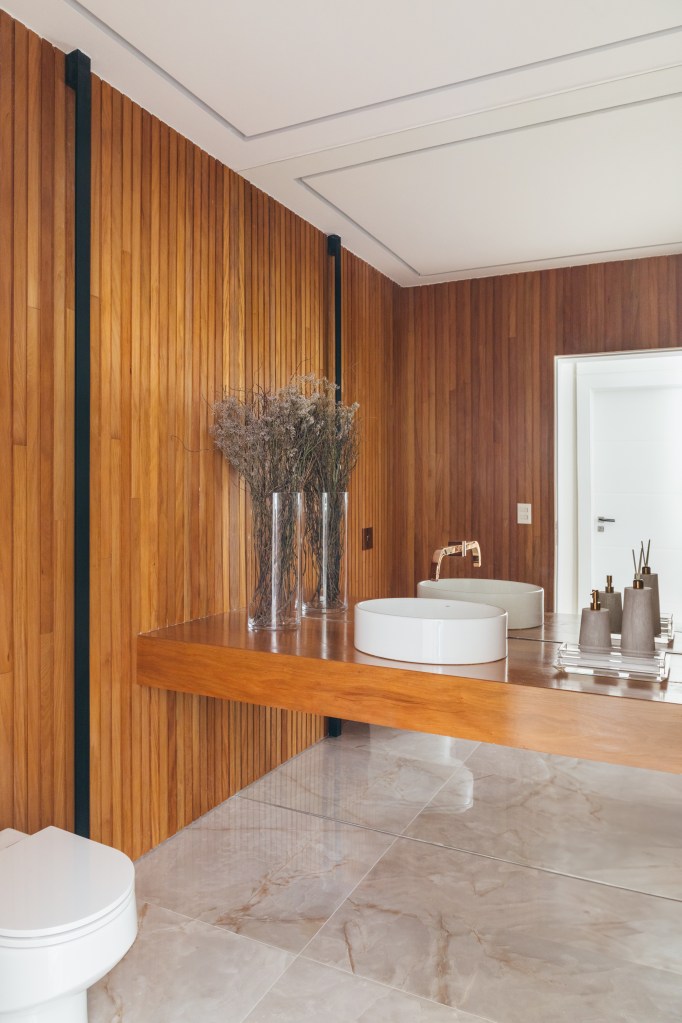 Projeto de Júlia Marques. Na foto, lavabo com paredes revestidas de madeira, bancada de madeira e cuba branca solta.