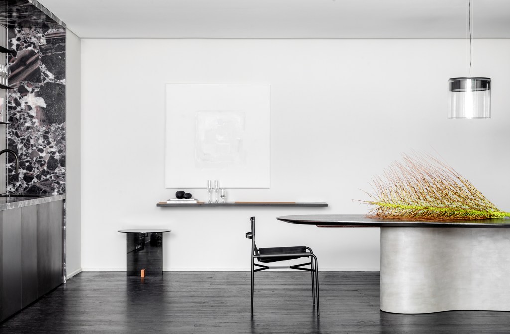 Madeira ebanizada é protagonista desta sala com décor branco e preto. Projeto de Barbara Ramos para a CASACOR Santa Catarina 2023. Na foto, sala de jantar com mesa curva, quadro e prateleira.