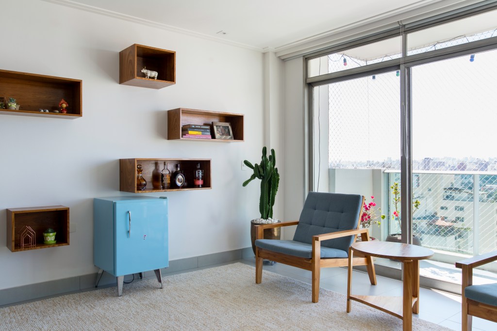 Projeto de Raízes Arquitetos. Na foto, sala de estar com tapete cinza, poltrona azul, frigobar azul e nichos na parede.