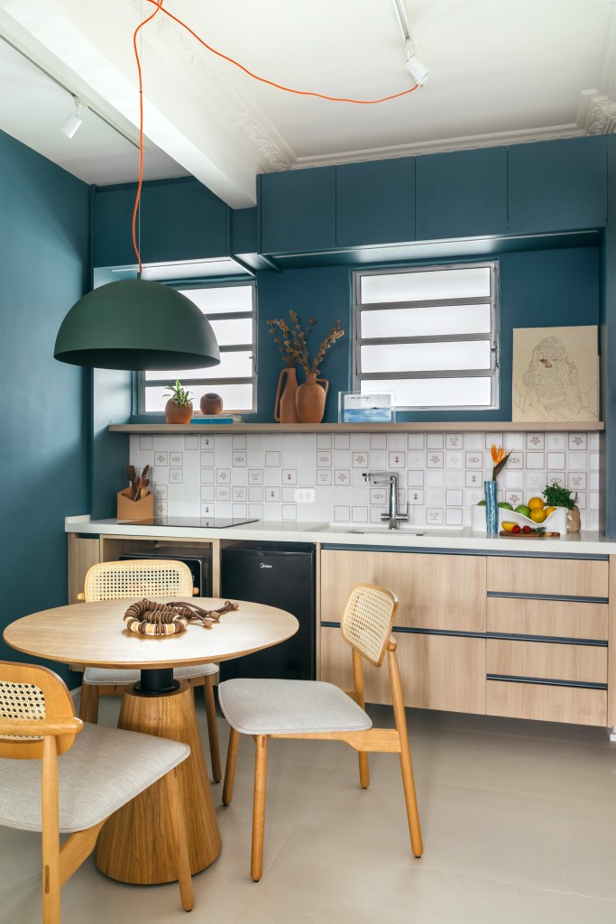 Projeto de Casa Cururu. Na foto, cozinha pequena com parede e marcenaria azul, bancada branca, prateleira e armário emoldurando janela.