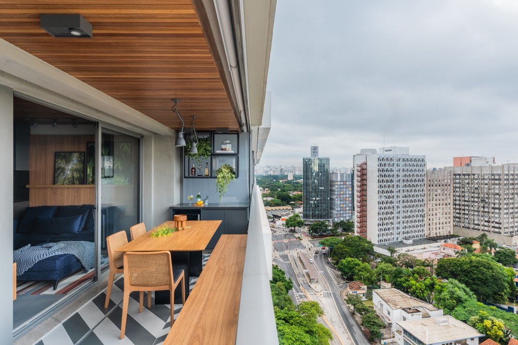 Apê de 64m² tem cozinha com bancada de mármore e forro de madeira. Projeto de Pietro Terlizzi. Na foto, varanda com mesa, cadeiras e piso geométrico preto e branco.