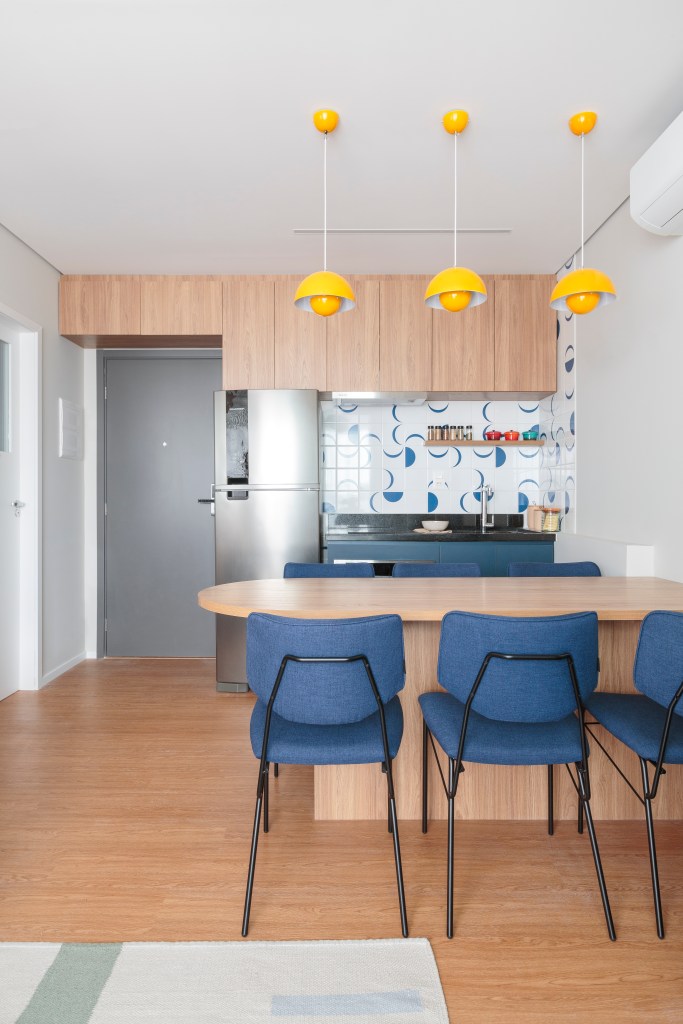 Projeto de Estúdio Maré. Na foto, cozinha integrada com parede de azulejos e bancada com cadeiras azuis.