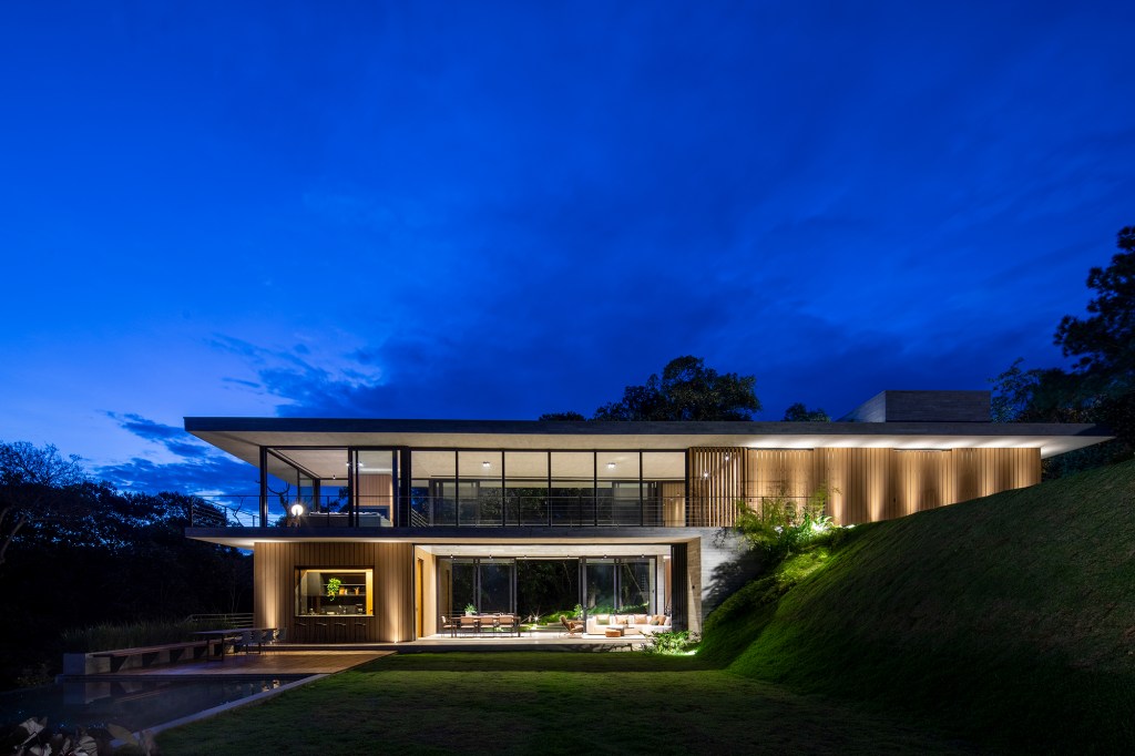 Casa de campo imersa na natureza parece flutuar em meio ao verde. Projeto de Conrado Ceravolo. Na foto, fachada e jardim. Sala com paredes de vidro.