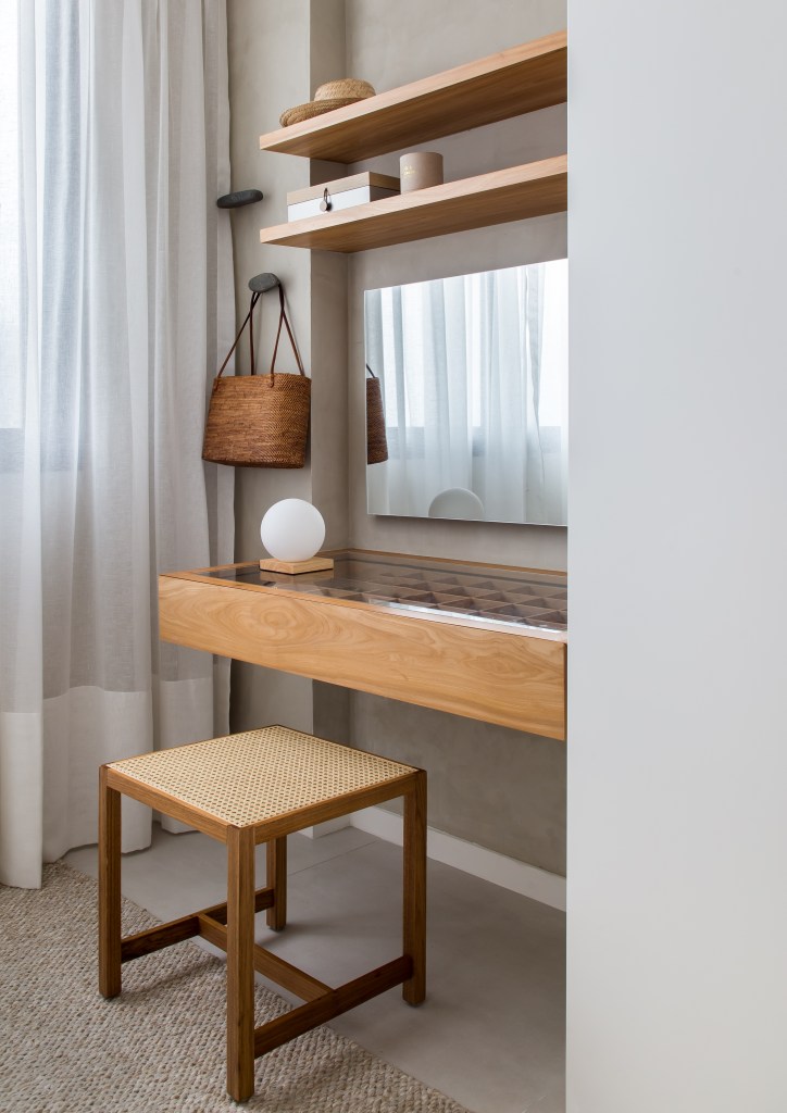 Décor essencial com branco e madeira peroba valoriza o mar neste apê. Projeto de PKB Arquitetura. Na foto, penteadeira pequena, banco de madeira, mesa com armazenamento e divisórias.