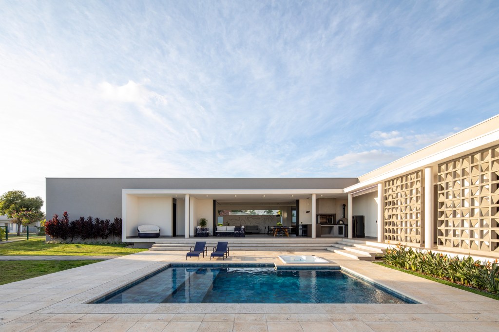 Fachada de cobogós cria efeito cênico nesta casa no interior de São Paulo. Projeto de Starq, Na foto, fachada da casa com piscina e jardim.