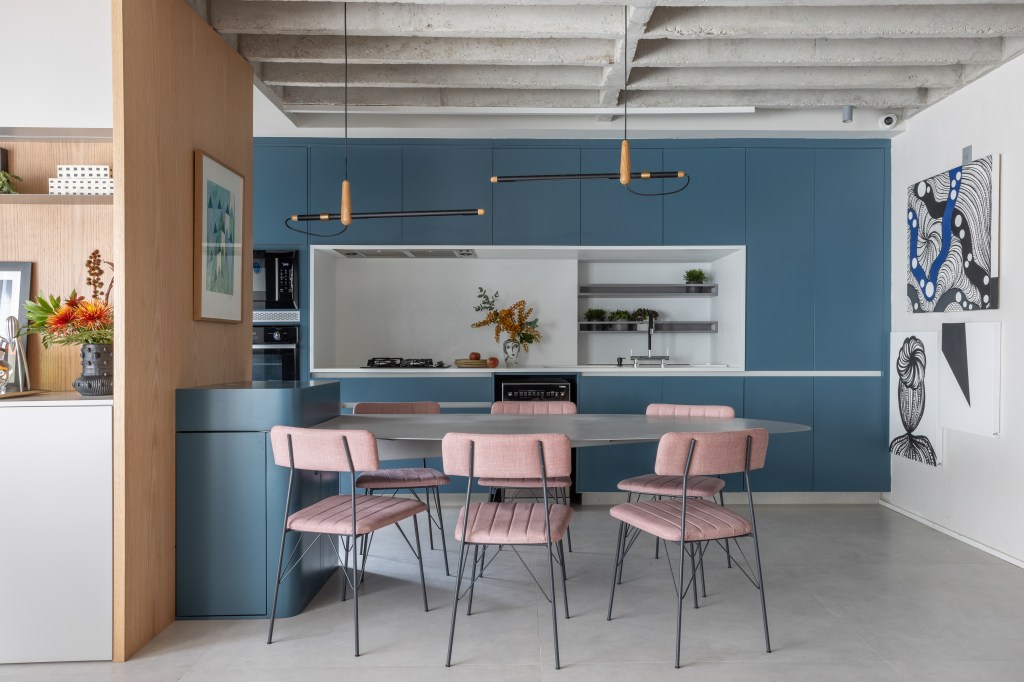 Laje de concreto, mesa em balanço e cozinha azul marcam apê de 115 m². Projeto do escritório Si Saccab. Na foto, cozinha integrada com mesa em balanço e marcenaria azul.