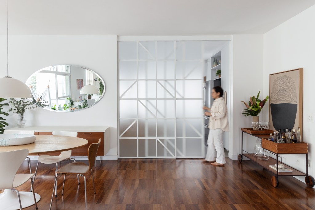 Com paleta branca, apê de 240 m² tem porta de correr inspirada em biombos. Projeto de Lucia Manzano. Na foto, sala, piso de madeira, porta de vidro de correr.