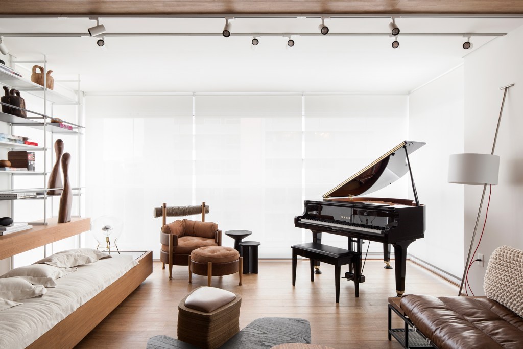 Apartamento de 150 m² une os hobbies do morador: piano, livros e filmes. Projeto de Nati Minas & Studio. Na foto, varanda com piano. sala de estar e jantar.