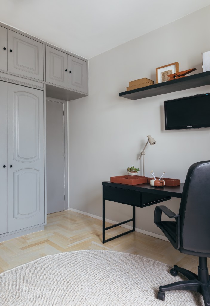 Apê de 160 m² em tons pastel alegres tem painel giratório de TV. Projeto de Ikeda Arquitetura. Na foto, home office com mesa preta e armário cinza.