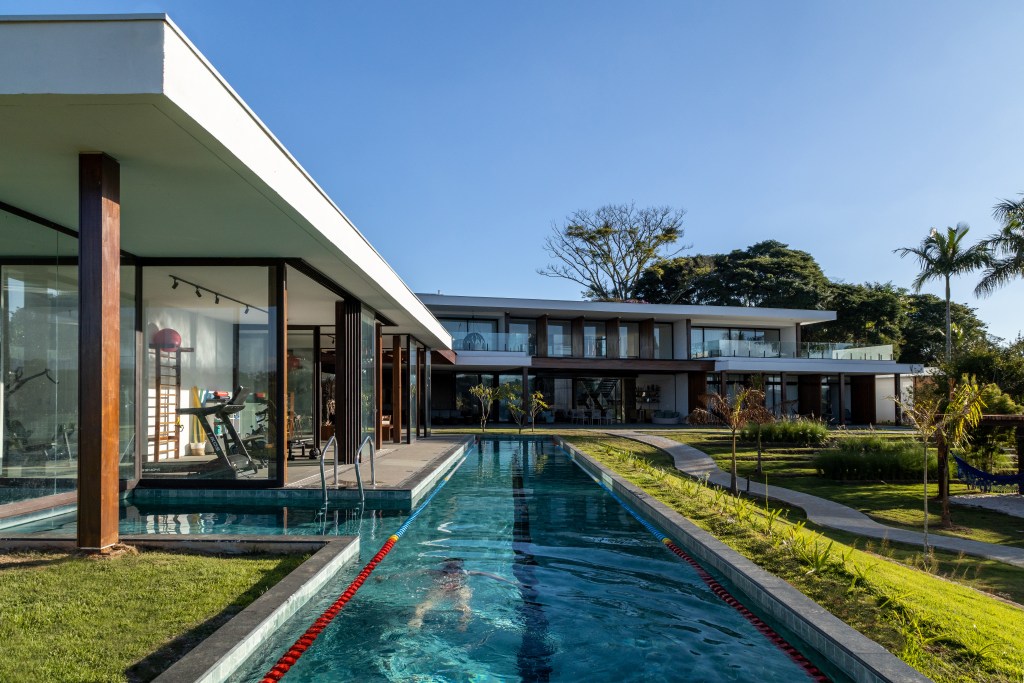 Casa é composta por três volumes ligados por pergolado de madeira. Projeto de Arkitito. Na foto, área externa de casa, raia, piscina.