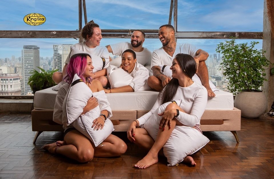 Porque você deve começar a decorar o quarto pela cama. Na foto, grupo de pessoas sorrindo em colchão com grande janela ao fundo.