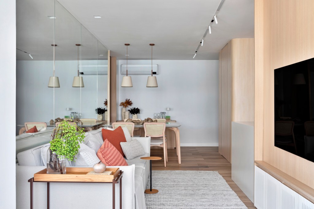 Espelho atrás do sofá amplia apê de 70 m² com paleta de cores clara